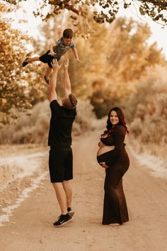 a man holding up a baby while standing next to a woman on a dirt road