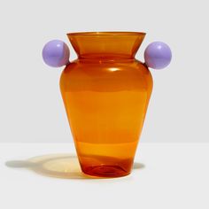 an orange glass vase with two balls on the top and bottom, against a white background