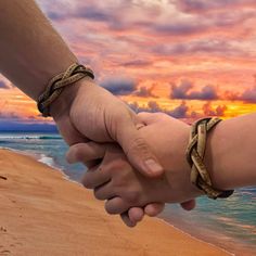 two people holding hands on the beach at sunset