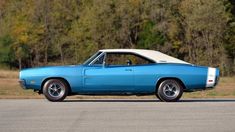 a blue and white muscle car parked on the side of the road with trees in the background