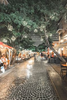 people are sitting at tables in the middle of an empty street with lights strung overhead