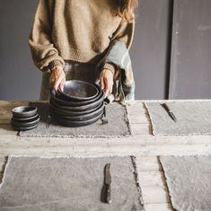 a woman standing over a stack of black plates