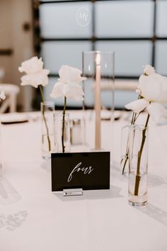 white flowers in vases on a table with a name card and place cards for guests