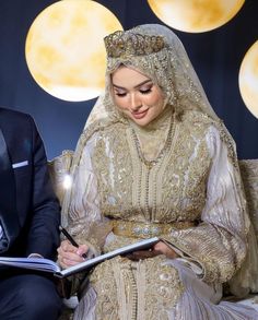 a man and woman dressed in wedding attire sitting on a couch with a notepad