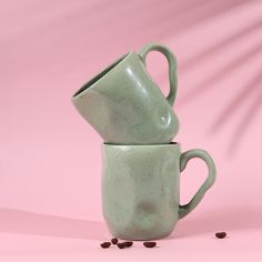 two green coffee mugs sitting next to each other on top of a pink surface