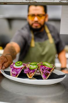 a man in an apron preparing food on top of a white plate with red cabbage and green peppers