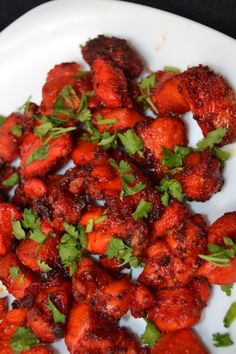 a white plate topped with sliced strawberries covered in cilantro and parsley