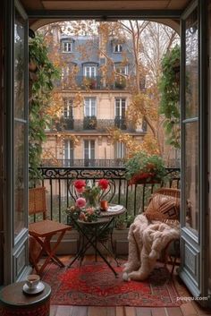 an open door leading to a balcony with furniture and flowers on the table in front of it