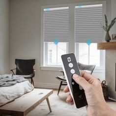 a person holding a remote control in front of a fireplace with blinds on the windows