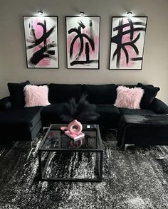 a living room with black couches, pink pillows and pictures on the wall above them