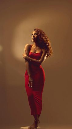 a woman in a red dress is posing for a photo with her arms crossed and looking off to the side