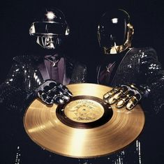 two people dressed in black and gold holding a golden record with their hands on it