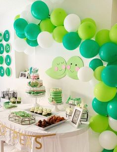 a table topped with lots of green and white balloons next to a wall filled with desserts