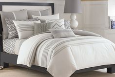 a bed with white and grey striped comforter in a bedroom next to a window