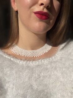 a close up of a woman wearing a white sweater with a necklace on her neck