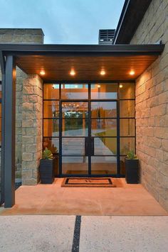 the front entrance to a modern home with glass doors and lights on it's sides