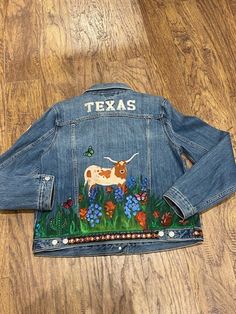 Custom handpainted  women's denim jacket (size large, 12-14) featuring a Texas longhorn and bluebonnets Spring Hand Painted Denim Outerwear, Spring Denim Outerwear Hand Painted, Spring Western Denim Outerwear, Hand Painted Blue Outerwear For Spring, Spring Rodeo Denim Jacket With Pockets, Hand Painted Blue Spring Outerwear, Blue Hand Painted Outerwear For Spring, Western Style Medium Wash Outerwear For Spring, Spring Denim Jacket With Pockets For Rodeo