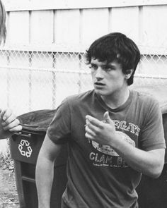 two young men standing next to each other in front of a trash can and fence