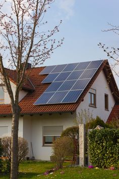 a house with a solar panel on the roof and some trees in front of it