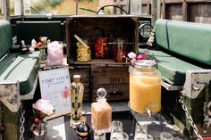 This shows a landscape shot of a drinks display for a wedding presented on the back of a land rover. The display consists of a glass dispenser with a yellow drink in it. At the fore front is a round tray with glasses of Prosecco. Next to the dispenser are bottles of alcohol. Behind them are crates stacked together with jars of fruit displayed. There is also a sign on the display that reads "Pimp your Prosecco" Wilderness Reserve, Vintage Crates, Reserved Seating