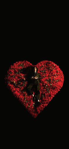 a man laying on top of a heart shaped bed of flowers in front of a black background