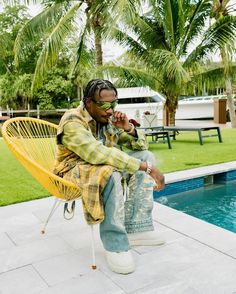 a man sitting in a chair next to a pool talking on a cell phone while wearing sunglasses