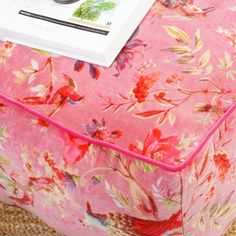 a close up of a pink flowered ottoman with a magazine on top of it