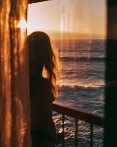 a woman standing on a balcony looking out over the ocean at sun setting in the distance