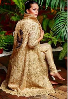 a woman sitting on top of a wooden bench wearing a gold dress and jacket with black polka dots