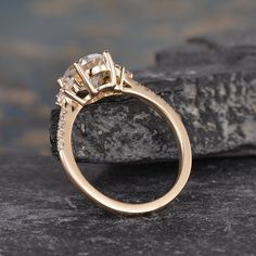 an engagement ring with three stones on top of it, sitting on a rock next to some rocks