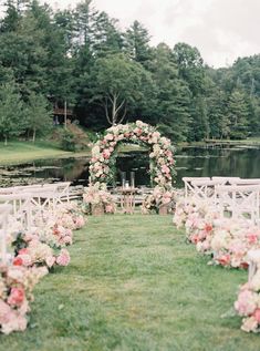 an outdoor wedding ceremony setup with white chairs and pink flowers on the aisle, surrounded by greenery