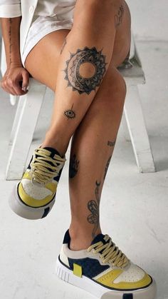 a woman sitting on a chair with tattoos on her legs and feet, wearing yellow sneakers