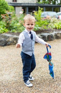 a little boy that is standing in the dirt holding an umbrella and smiling at the camera