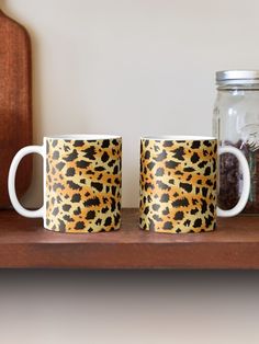 two leopard print coffee mugs sit on a shelf next to a jar with coins