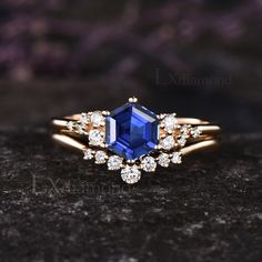 a blue sapphire and diamond ring sitting on top of a black stone surface with purple flowers in the background