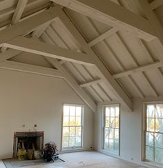 an empty room with two windows and a fire place in the center, surrounded by wood beams