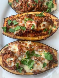 three stuffed eggplant boats with meat, cheese and herbs on white plate sitting on table