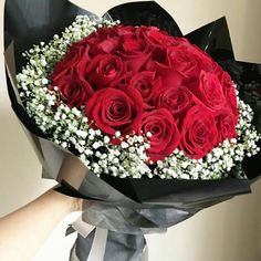 a bouquet of red roses and baby's breath is held by someones hand