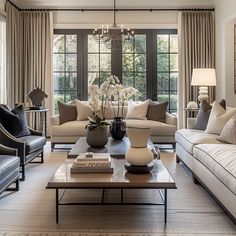 a living room filled with furniture and a chandelier hanging from the ceiling in front of two windows