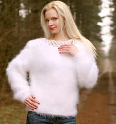 a blonde woman wearing a white sweater and jeans posing for a photo in the woods