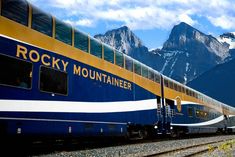 the rocky mountaineer train is moving along the tracks in front of snow capped mountains