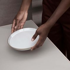 a person holding a white plate on top of a table with their hand over it