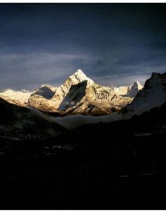 the mountains are covered in snow under a dark sky with clouds and sun shining on them