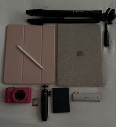 an ipad, camera, notebook and other items laid out on a bed