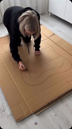 a woman bending over on top of a cardboard box that is taped to the floor