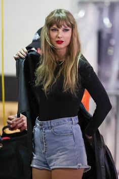 a woman in high waisted denim shorts and black shirt with red lipstick standing next to a handbag