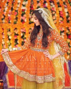 a woman in an orange and yellow outfit with flowers on the wall behind her,