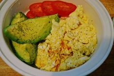 a white bowl filled with eggs, tomatoes and cucumber slices on top of a wooden table