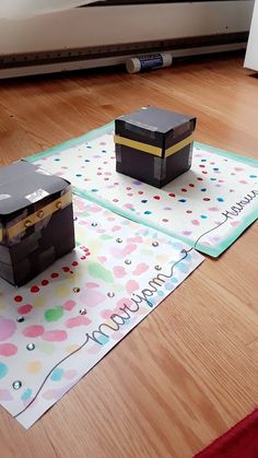 two small boxes sitting on top of a mat in the middle of a wooden floor