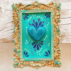 a blue heart in a gold frame on a wooden table with white paint and wood planks